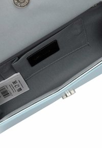 Intérieur d'un sac à main bleu clair avec doublure en tissu gris, une étiquette blanche avec code-barres, et une petite fermeture ronde en argent sur le bord extérieur.