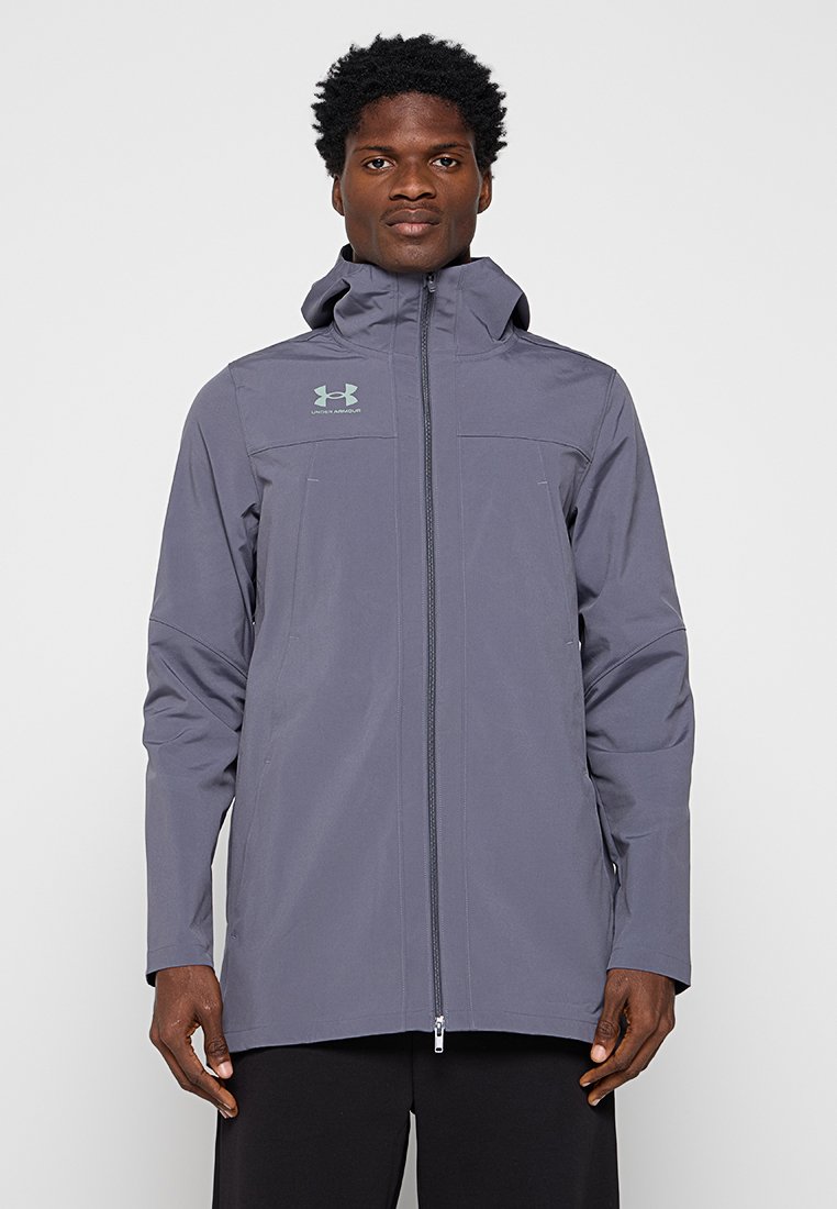 Veste grise résistante aux intempéries avec un col haut et une fermeture éclair intégrale. Elle possède des poches et le logo Under Armour dans un vert clair contrastant.