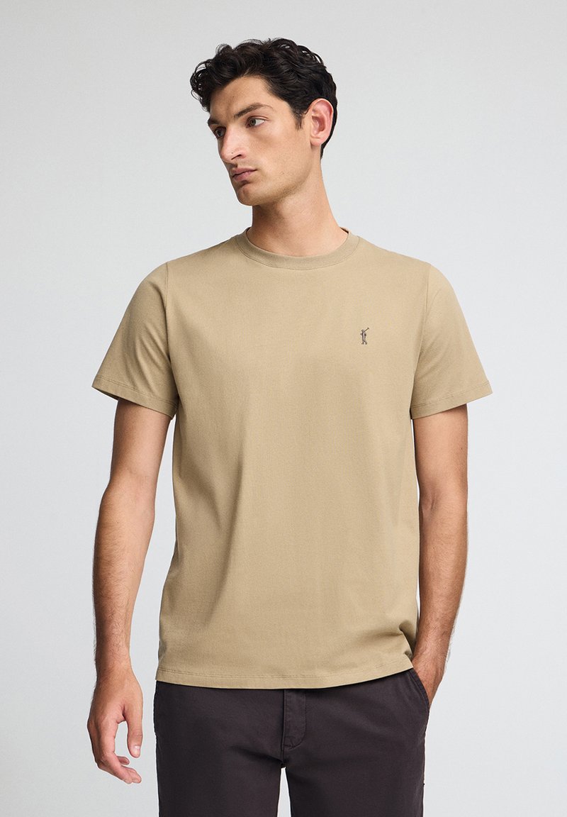 Beżowa koszulka z bawełny z okrągłym dekoltem i krótkimi rękawami. Posiada małe haftowane logo na lewej piersi. Gładka faktura.