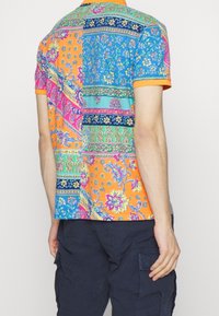 Kortärmad skjorta med ett lapptäckesdesign i livfulla orange, blå och rosa mönster. Texturerat tyg med krage.