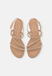 Sandali beige con più sottili cinturini, caratterizzati da decorazioni in cristallo e una fibbia dorata. Design piatto con una soletta in pelle liscia.