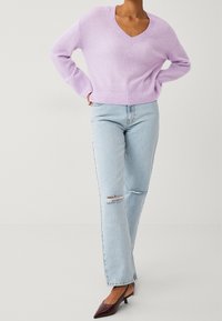 Maglione viola chiaro con scollo a V, orlo a coste, abbinato a jeans azzurri con ginocchia rovinate e scarpe con tacchi bordeaux scure.