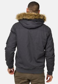 Chaqueta gris con capucha y ribete de piel sintética, con cierre de cremallera en la parte frontal, puños acanalados y un bolsillo en la manga izquierda. Fabricada con un tejido duradero y diseño de corte relajado.