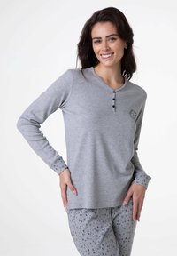 Maglia grigia a maniche lunghe con collo henley abbottonato, caratterizzata da una piccola grafica e da polsini decorati. Abbinata a pantaloni da pigiama coordinati, arricchiti da motivi a stella.