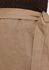 Beige linen fabric with a textured surface, featuring a wide waistband and a silver buckle accent, secured with a tied belt.