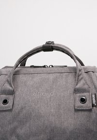 Sac à main en tissu gris avec deux poignées maintenues par un bouton-pression noir et le nom de la marque "anello" brodé à l'avant.
