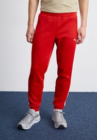 Røde joggebukser med hvite stripesider, laget av glat materiale. Har en avslappet passform og elastisk midjebånd med lommer.