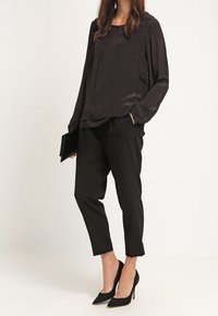 Svart sidenblus med rund halsringning, tillsammans med skräddarsydda svarta byxor med smal passform. Bärs med svarta högklackade skor.