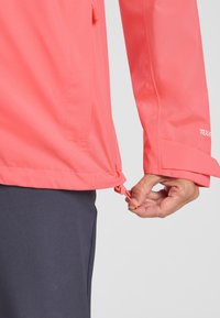 Giacca impermeabile corallo con orlo regolabile. Presenta una texture liscia, maniche lunghe e un cordoncino regolabile per una vestibilità personalizzata.