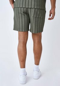 Pantaloni corti a righe verdi realizzati in tessuto testurizzato, dotati di una tasca posteriore. Abbinati a sneakers bianche e calze.