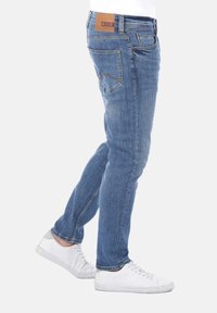 Jeans de mezclilla azul claro con corte ajustado, con un parche trasero de cuero marrón, cinco bolsillos y detalles de costura sutiles.