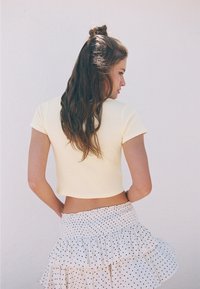 Kroppad gul t-shirt med korta ärmar, kombinerad med en prickig kjol med volanger. Fokus på textur och färgkontrast.