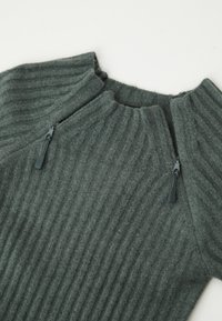 Pullover a coste in verde scuro con collo alto e due zip laterali. Texture morbida con un design strutturato.