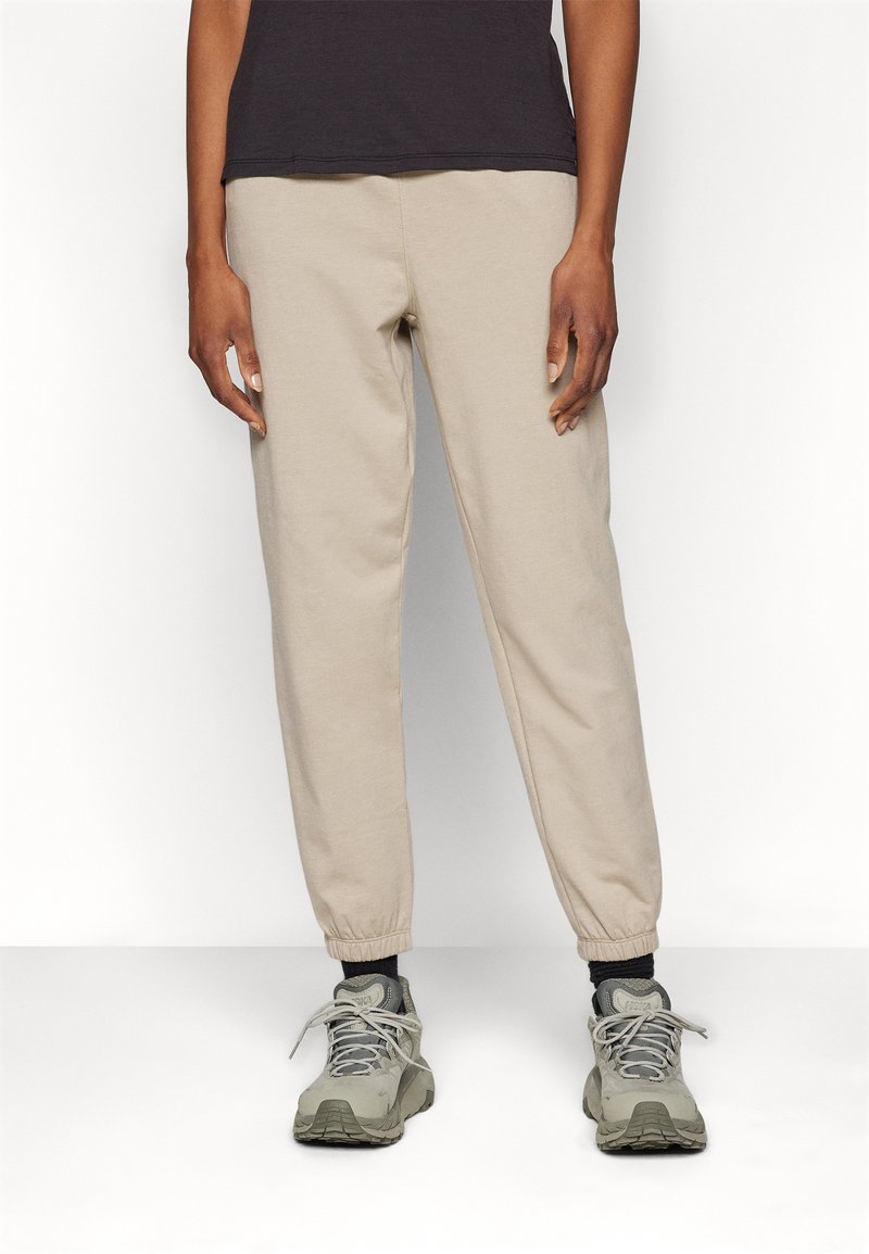 Beige Baumwoll-Sweatpants mit einem elastischen Bund und Bündchen, kombiniert mit grauen Sneakers. Der Stoff hat eine glatte Textur und eine lockere Passform.