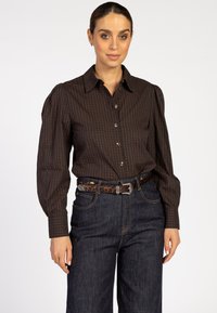 Bruine geruite blouse met pofmouwen, gecombineerd met hooggesneden donkere spijkerbroek en een bruine luipaardprintriem.