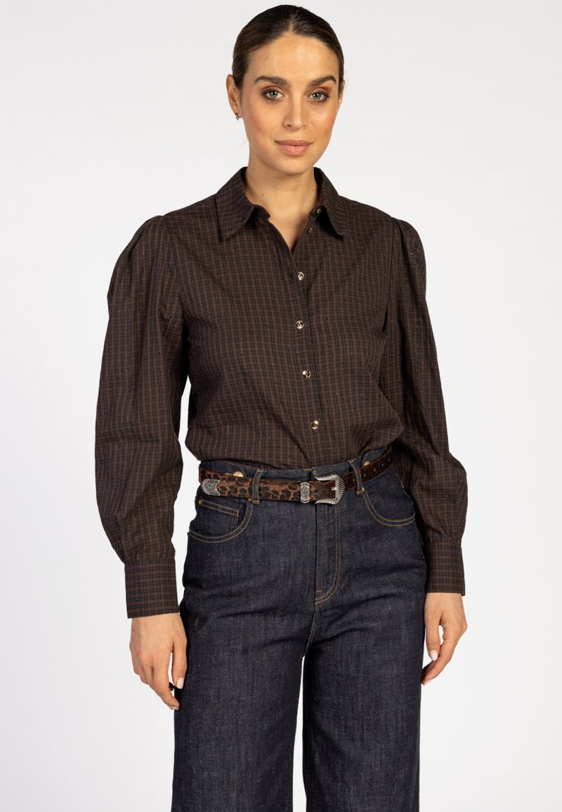 Bruine geruite blouse met pofmouwen, gecombineerd met hooggesneden donkere spijkerbroek en een bruine luipaardprintriem.