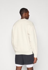 Sweatshirt couleur crème avec des poignets et un ourlet côtelés, offrant une coupe décontractée. Porté par-dessus un short noir, montrant un design simple et une texture douce.