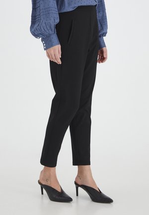 Pantalon noir ajusté avec poches avant, coupe slim, et texture lisse, associé à des mules noires texturées, porté avec un chemisier bleu clair.