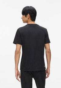 Melna apkakles T-kreklu ar īsām piedurknēm, gluda tekstūra un brīva piegriezuma. Satur mazu logotipu apakšējā malā.