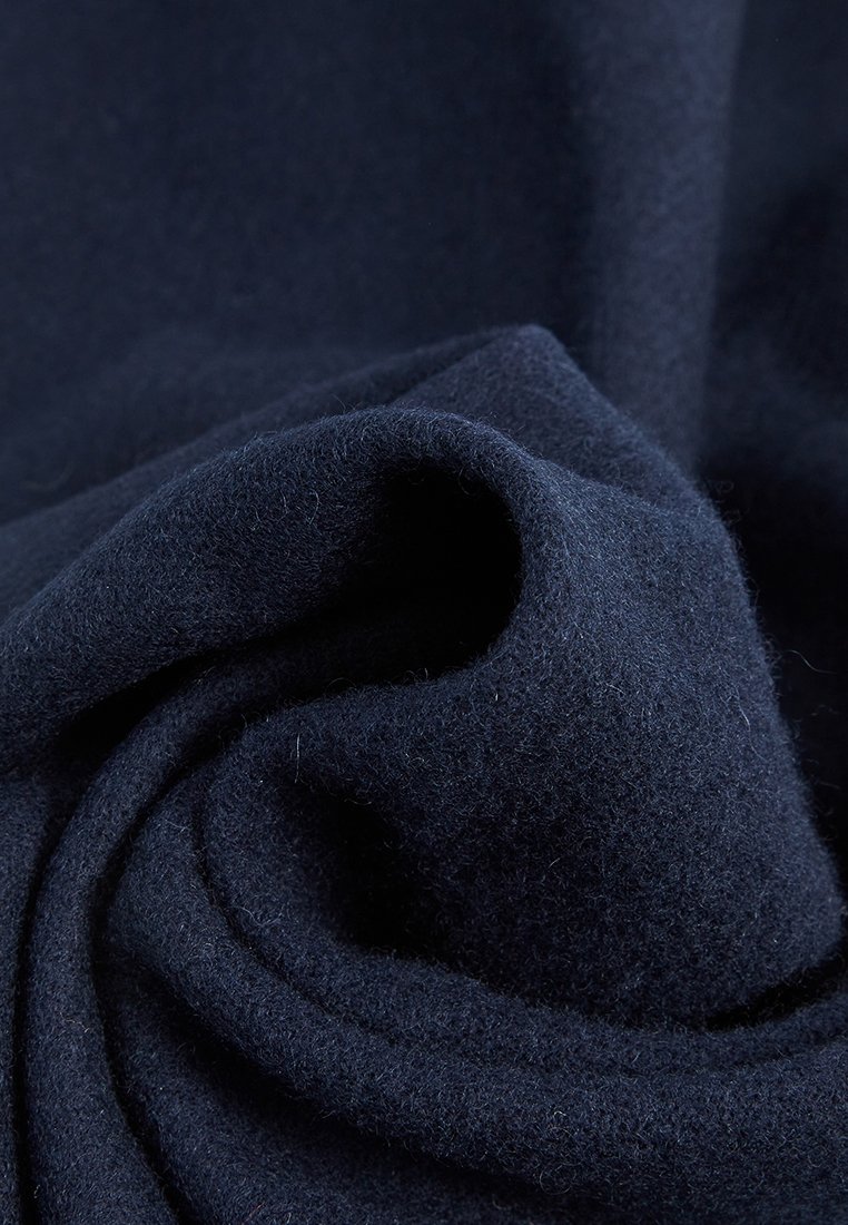 Tessuto di lana blu navy con una consistenza morbida e pelosa, piegato in un motivo a spirale largo, che evidenzia la sua densità e calore.