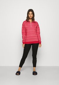 Rød genser med kvart glidelås og mønsterdesign, kombinert med svarte leggings og marineblå tøfler. Glatt stoff og avslappet passform.