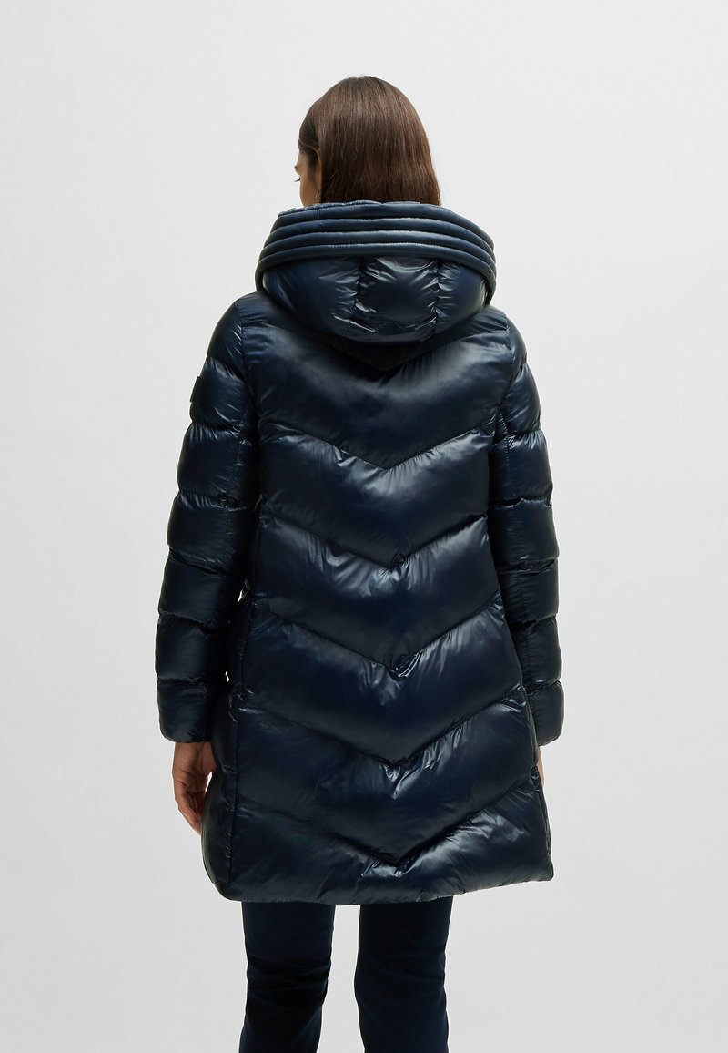 Granatowa kurtka puchowa z kapturem, charakteryzująca się błyszczącą teksturą, wzorem w romby oraz podwyższonym kołnierzem ściąganym w celu zapewnienia dodatkowego ciepła.