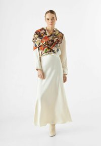 Zijde sjaal met levendige bloempatronen over een crèmekleurige satijnen jurk; soepele textuur, enkellange ontwerp, gecombineerd met lichte laarzen.