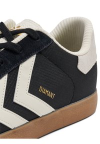 Pantof sport negru cu design alb în formă de chevron, partea superioară texturată, talpă de cauciuc, accente bej și text auriu „DIAMANT” pe lateral.