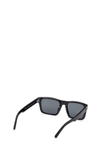Occhiali da sole neri rettangolari con lenti grigie scure. Montatura in plastica lucida, aste dritte e dettaglio in metallo argentato vicino alle cerniere.
