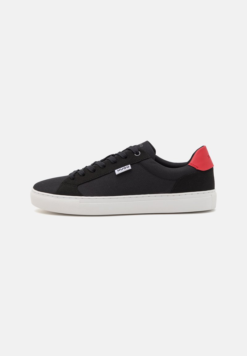 Svart sneaker med en texturerad ovandel, vit sula och röd hälaccent. Har runda skosnören och en liten varumärkesskylt på sidan.