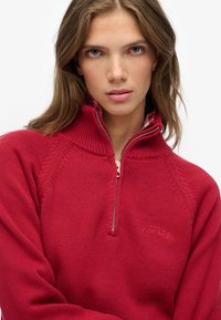 Czerwona bluza na zamek z prążkowanym kołnierzem i fakturowanym splotem. Z logo na piersi i kratkowaną tkaniną na krawędzi kołnierza.