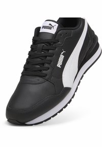 Černé kožené tenisky s bílými akcenty, mají texturovaný povrch, šněrovací design, polstrovaný límec a černou gumovou podrážku. Zobrazené logo PUMA.