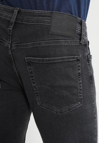 Los vaqueros de mezclilla negra cuentan con una cintura de medio tiro, bolsillos traseros con detalles sutiles de costura y un acabado de tela texturizada.