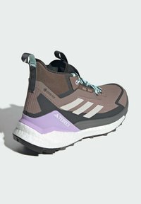 Ruskeat ja mustat retkeilykengät, joissa on tekstuuri verkko päällinen, valkoiset raidat, vaaleansiniset nauhat ja violetin värinen välipohja. Gore-Tex-logo näkyvissä.
