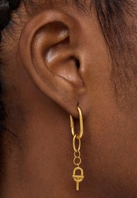Pendiente de aro de oro con un diseño de eslabones de cadena y un acento tipo cierre en la parte inferior. Textura suave con un acabado pulido.