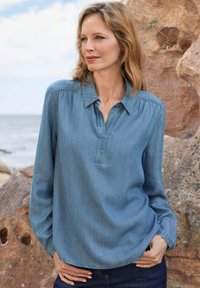 Helleblaue Jeanshemd mit langen Ärmeln, Knopfkragen und teilweisem Knopfleisten. Weiche Textur mit lässigem Schnitt, kombiniert mit dunklen Jeans.