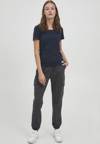 Mörkblå t-shirt kombinerad med grå joggerbyxor med cargo-fickor och elastiska mudd, bärs med vita sneakers. Avslappnad, bekväm passform.