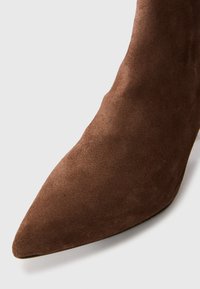 Botín de ante marrón hasta el tobillo con punta afilada y superficie lisa. Presenta un diseño elegante y ajustado sin hardware o acentos visibles.