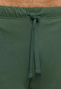 Pantaloni corti verdi in cotone con vita elasticizzata e cordoncino annodato. Il tessuto ha una consistenza liscia senza motivi visibili.