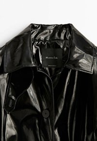 Veste en similicuir noir brillant avec un large col et un seul bouton visible, portant l’étiquette de la marque Massimo Dutti à l’intérieur de l’encolure.