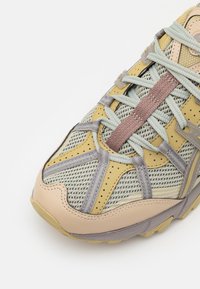 Träningsskor med ovandel i nät i gult och grått, med texturerade detaljer, ljusblå snören och en solid beige mellansula.