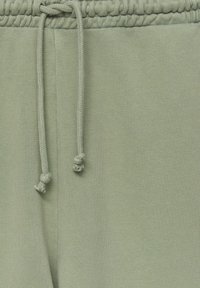 Lichtgroene sweatpants met een gestructureerde stof, voorzien van een elastische tailleband en een trekkoord met geknoopte uiteinden. Geen zichtbare zakken.