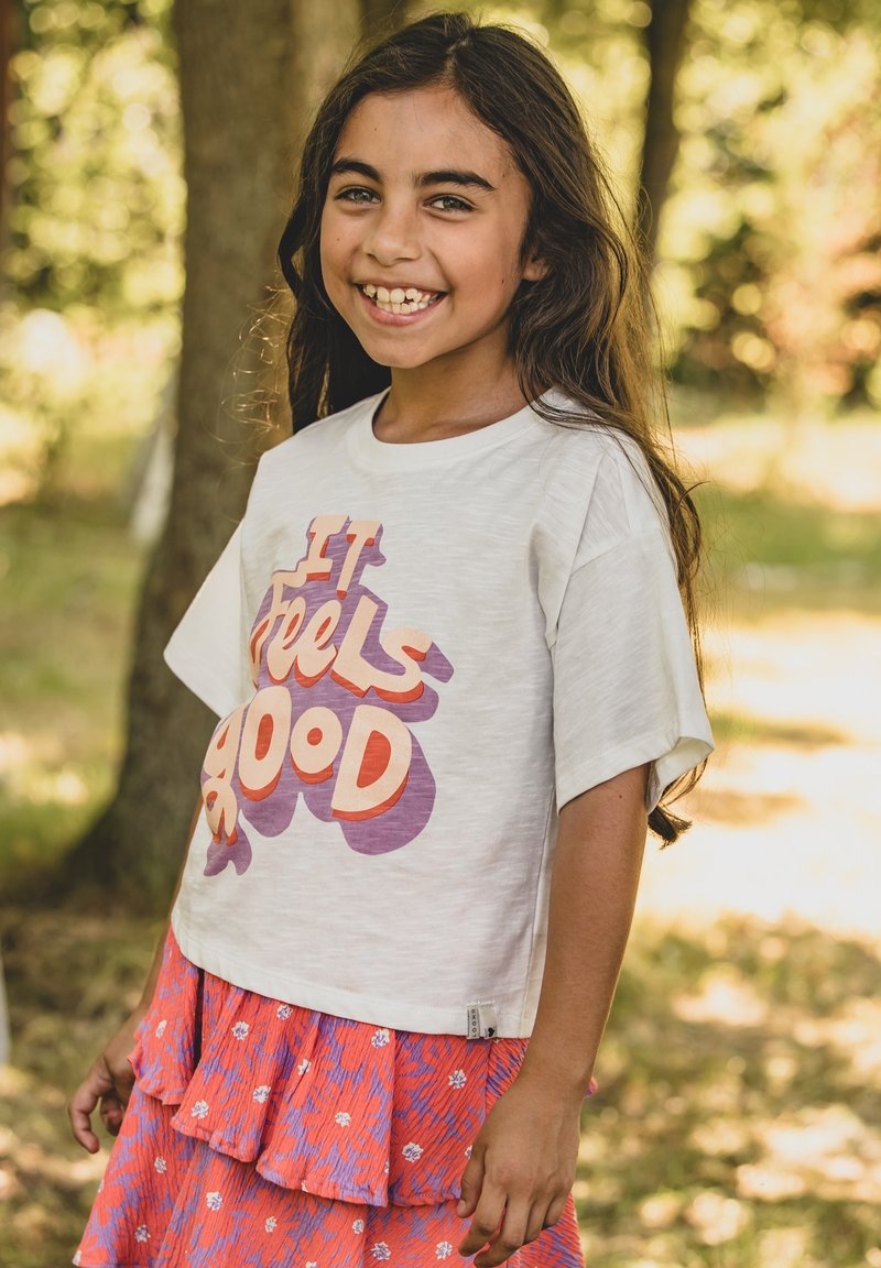 Wit katoenen T-shirt met oversized mouwen, voorzien van de tekst 'It Feels Good' in meerkleurige letters. Gecombineerd met een gelaagde, roze bloemenrok.