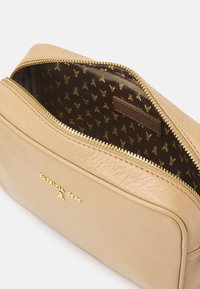 Borsa cosmetica in pelle beige con zip dorata, con un interno marrone a motivo e un marchio in rilievo sul fronte.
