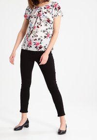 Floral blouse with short sleeves in a white fabric, featuring pink and blue flowers; paired with black skinny pants and black flats.