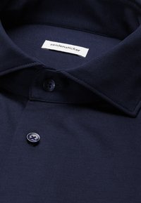 Polo bleu marine à col avec deux boutons foncés et une étiquette blanche portant l'inscription « seidensticker » à l'intérieur du col.