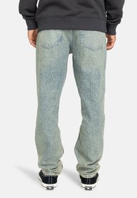 Vaqueros de mezclilla de un azul claro y holgados, con un acabado desgastado, que presentan dos bolsillos traseros y dobladillos remangados, combinados con zapatillas negras.