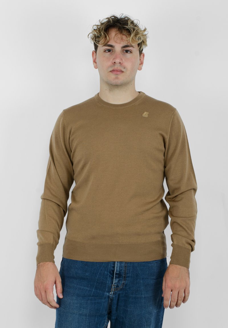 Maglione lungo marrone a maniche lunghe con collo rotondo e polsini a coste, realizzato in materiale morbido. Dettaglio del logo piccolo sul lato sinistro del petto.