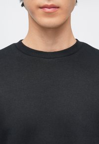 Fekete, kerek nyakú pulóver puha anyagból. Az anyag textúrája simának tűnik, bordázott nyakkivágással, látható minták vagy grafikák nélkül.