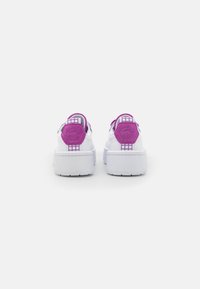 Weiße Sneaker mit lila Akzenten, ausgestattet mit einer strukturierten Ferse, einem gemusterten Detail am Kragen und einer dicken, erhobenen Sohle.
